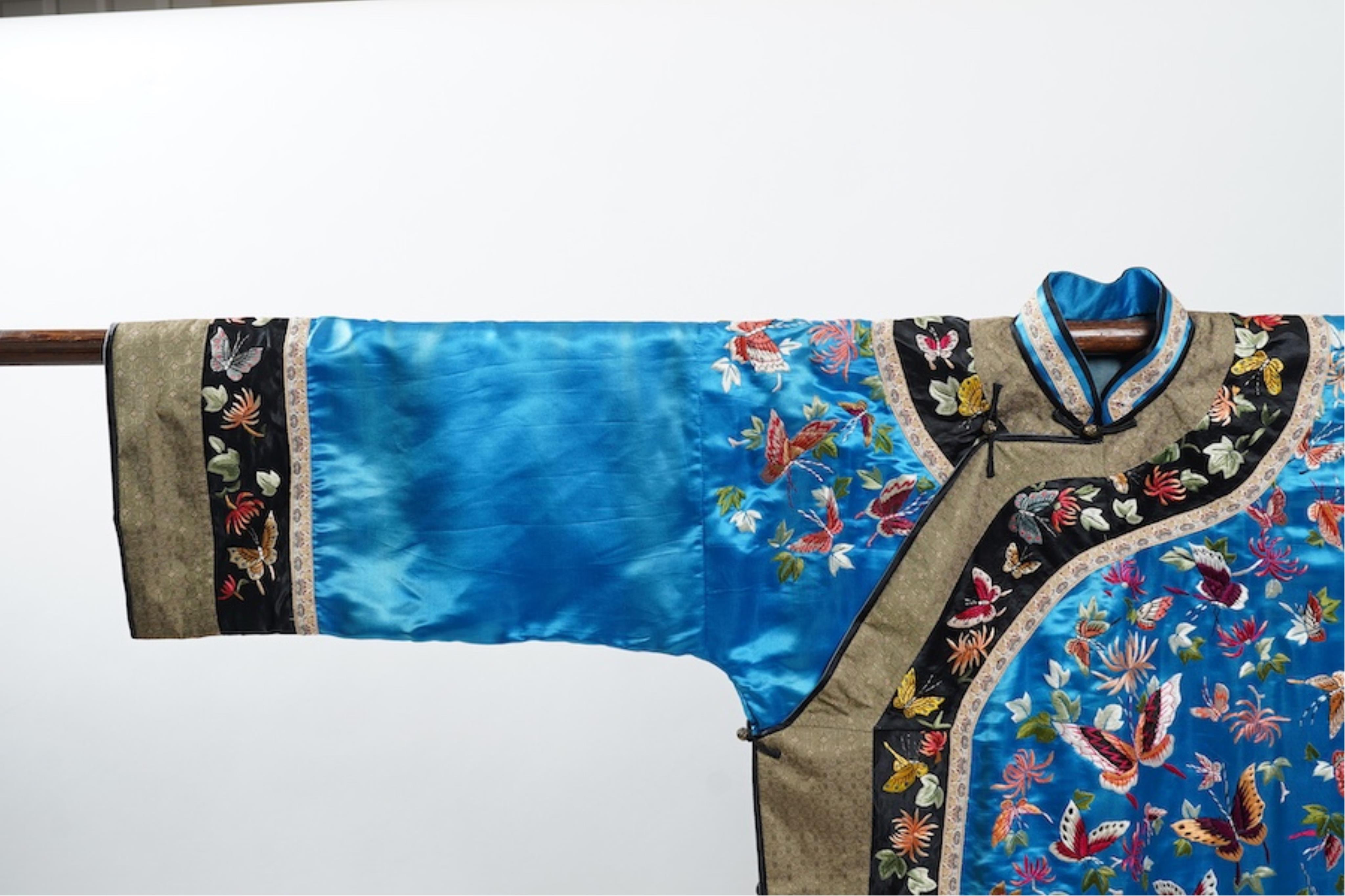 A mid 20th century Chinese turquoise silk jacket, with all over polychrome butterfly embroidery, similar embroidered sleeve bands, front and bottom edges on black silk, all bordered with gold brocade. The jacket blue sil